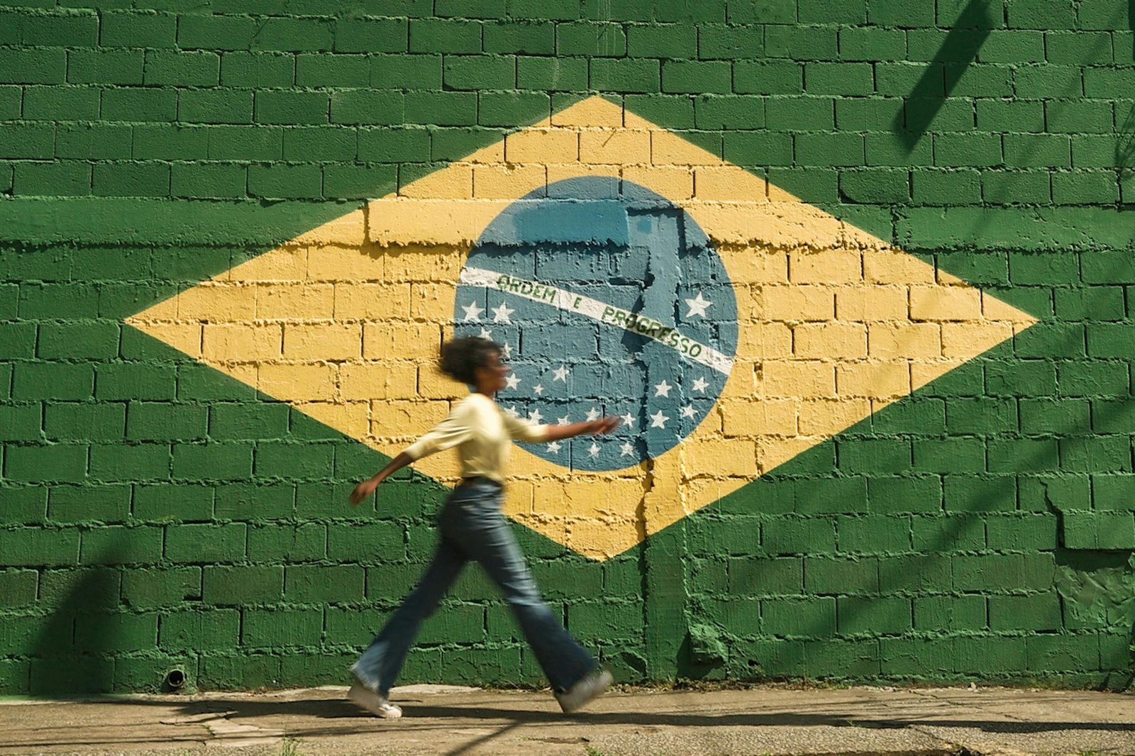 African American girl walking by a Brazilian flag mural on a sunny outdoor street.